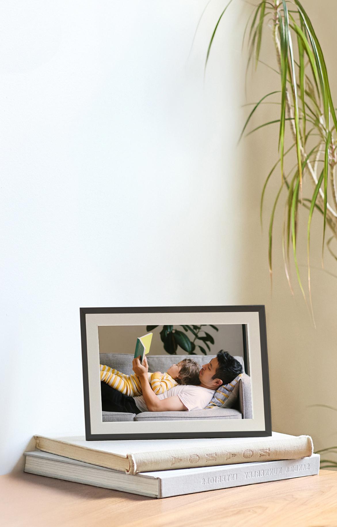 An Aura frame styled on top of books on a tabletop.