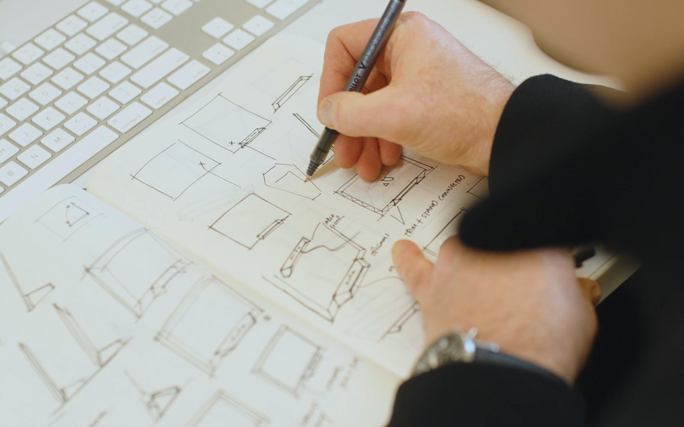 Hand sketching picture frame design concepts in a notebook.
