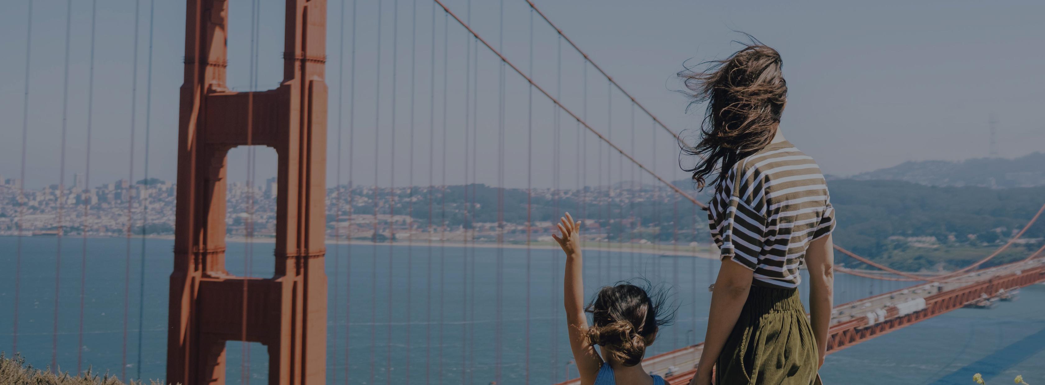 A mother and daughter waving at the Golden Gate Bridge.